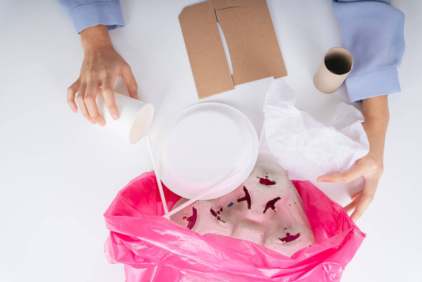 Nainen käsi puhdistaa elintarvikepakkauksen jätteet muovipussiin kierrätysmenettelyä varten. - Valokuva, kuva