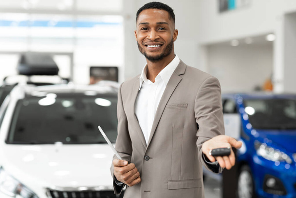 Car Dealer Offering Automobile Key To Camera Standing In Dealership - Photo, Image