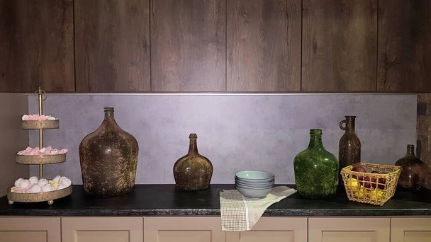 Большие стеклянные вазы, корзина с яблоками и тарелками в интерьере современной кухни. Сочетание дерева и бетона в конструкции. Кухня в современном стиле
. - Фото, изображение