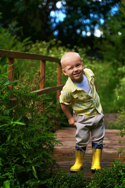a little boy in yellow boots and a yellow shirt winks. - Foto, imagen