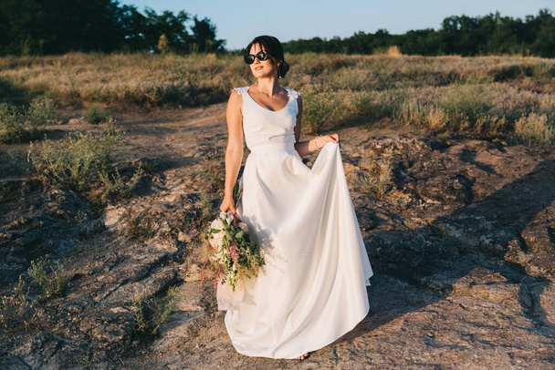 La sposa in un lussuoso abito da sposa bianco e occhiali in natura al tramonto - Foto, immagini
