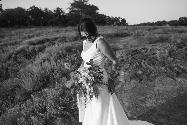 La sposa in un lussuoso abito da sposa bianco e occhiali in natura al tramonto - Foto, immagini
