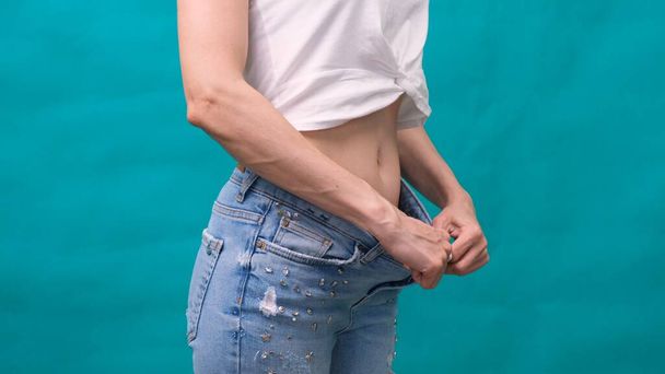 Aantrekkelijke jonge vrouw draagt jeans en toont slank lichaam na sport trainingen en gezond eten. Gewichtsverlies concept. - Foto, afbeelding