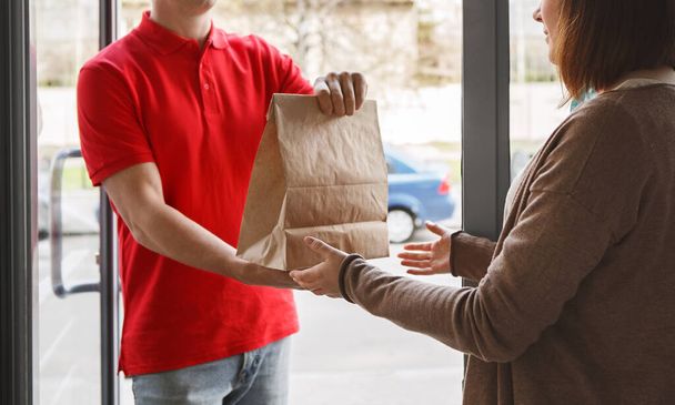 Delivery with courier at home. Deliveryman gives paper package to girl client - 写真・画像