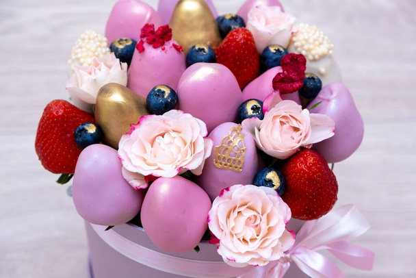 Fragole fresche in cioccolato rosa, oro e bianco con fiori rosa sotto forma di bouquet di frutta. - Foto, immagini
