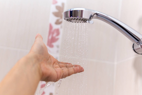 handen controleren de temperatuur van het douchewater. de hand van een man onder een stroom van water selectieve focus - Foto, afbeelding