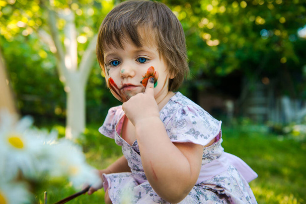 little girl is drawing. Young artist. Painting.  Funny girl in the park. activity for children. funny girl painted her face. Dirty face  - Photo, Image