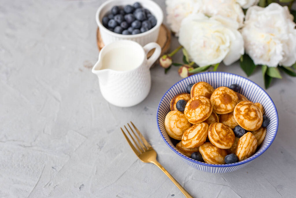 Mini cereal pancakes with blueberries in a bowl on gray background. Trendy food concept, Breakfast time for kids. Menu, recipe, top view or flat lay - Photo, Image