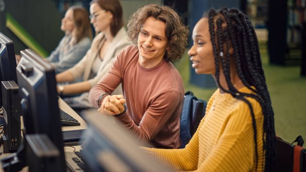 Row of Computer in University Library: Focused Bright Caucasian Boy and Talented Black Girl Study for Exams, Work on Assignment, Point at the Screen, Talk, Look for Solution, Explain Subject - 写真・画像