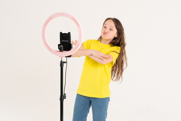 Teinityttö tanssii ja kuvaa videon. Selfietä. Puhelin on asennettu jalustalle ja rengaslamppu loistaa
 - Valokuva, kuva