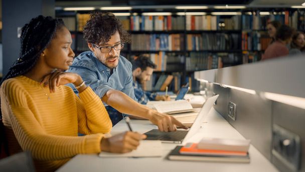 University Library: Gifted Black Girl uses Laptop, Smart Classmate Explains and Helps Her with Class Assignment. Study for Class Writing Paper Assignment. Diverse Students Learning, Studying for Exams - Foto, afbeelding
