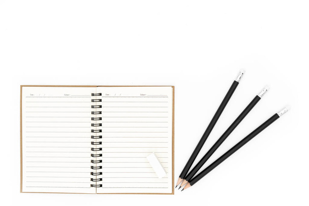 Guma je umístěna na otevřeném zápisníku a tužka je umístěna na pravé straně zápisníku, vše na bílém pozadí. - Fotografie, Obrázek
