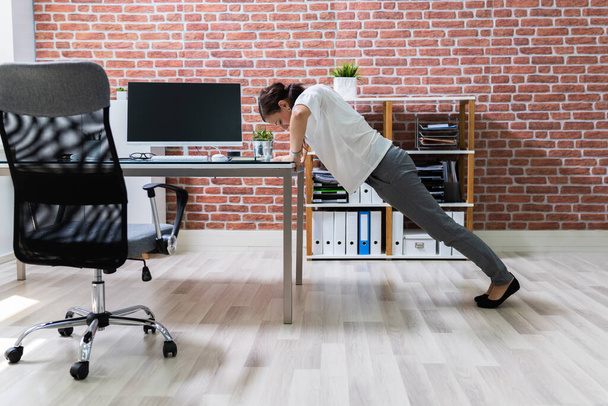 Πλάγια άποψη μιας νεαρής επιχειρηματία κάνει push up στο γραφείο - Φωτογραφία, εικόνα