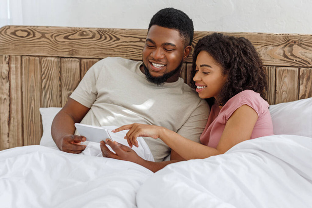 Fröhliches Paar mit neuer Handy-App im Bett liegend - Foto, Bild