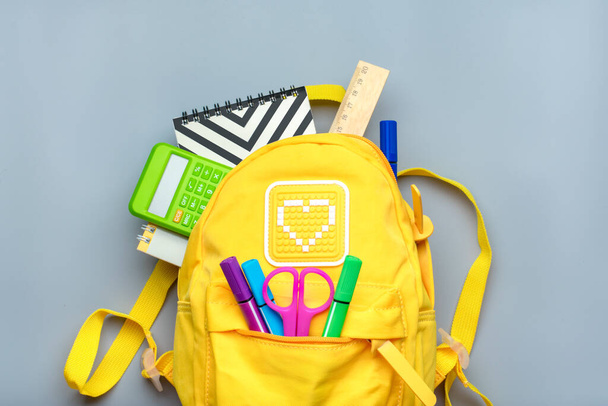 Back to school, education concept. Yellow backpack with school supplies - notebook, pens, ruler, calculator, scissors isolated on gray background. Top view. Copy space Flat lay composition Banner. - Photo, Image
