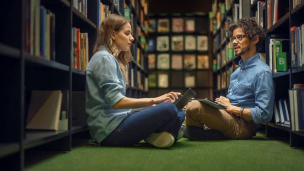 University Library: Smart Caucasian Girl Sitting and Talented Hispanic Boy Sitting Cross-Legged On the Floor, Talk, Use Laptops and Discuss Paper, Study and Prepare for Exams Together - Zdjęcie, obraz