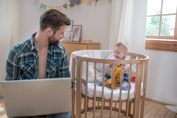 Dark-haired father working on a laptop while his little son playing - Photo, image