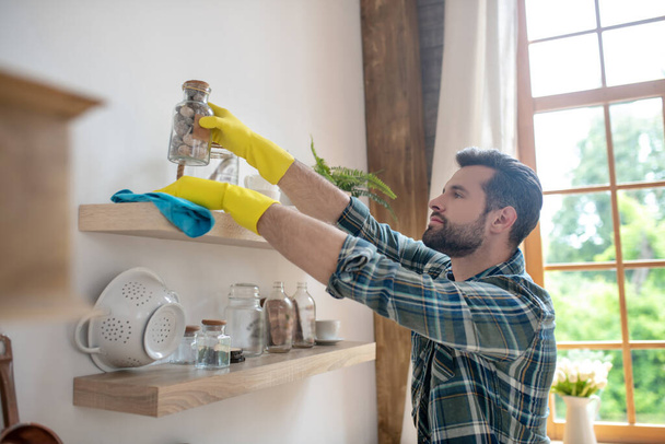 Dark-haired man in yellow gloves cleaning the kitchen - 写真・画像