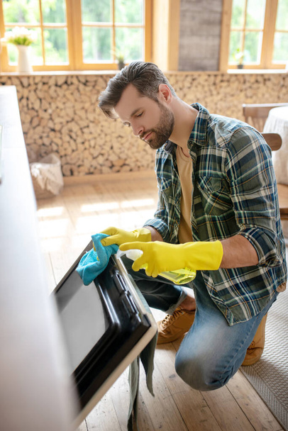 Mies keltaisissa käsineissä puhdistaa keittiön pintaa ja näyttää kiireiseltä - Valokuva, kuva