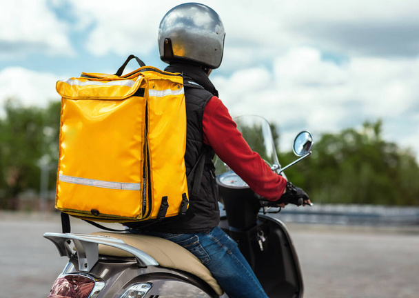 Corriere di consegna del cibo con lo zaino giallo che guida la moto all'aperto, vista posteriore - Foto, immagini
