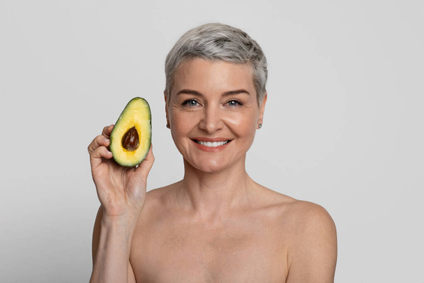 Эфирные масла для кожи и красоты. Привлекательная женщина средних лет, держащая авокадо наполовину
 - Фото, изображение