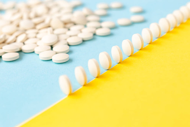 Abstract yellow-blue background,a scattering of pills,pills in a row stand on the edge like dominoes.Bright, conceptual.Healthcare, medicines.Fighting the virus, depression, headache. Calcium - Фото, зображення