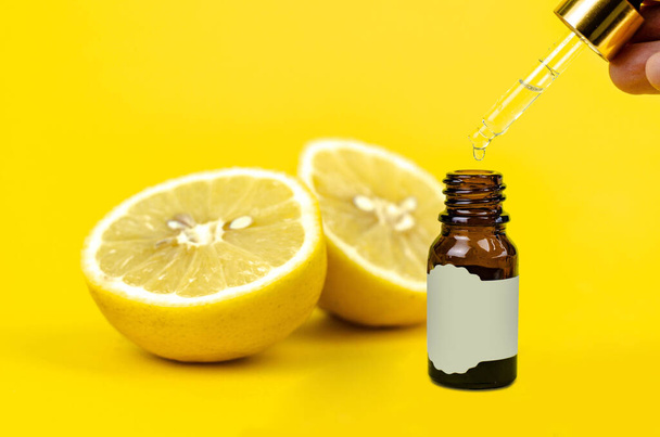 Pequeña botella de aceite esencial de limón con pipeta y gotas en la mano sobre fondo amarillo
 - Foto, imagen