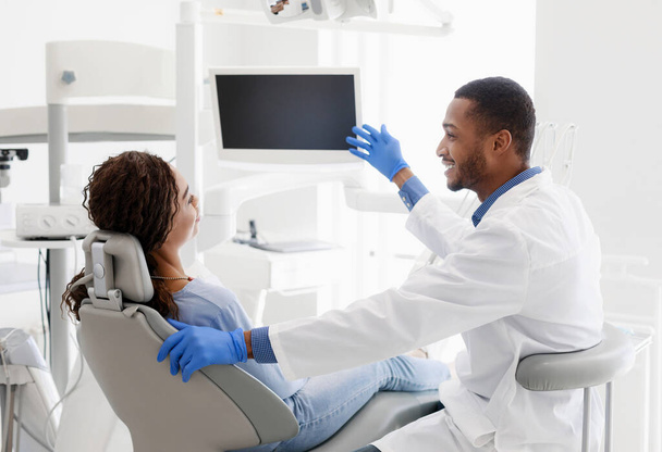 Afrykański dentysta rozmawia z pacjentem, wskazując na pusty monitor. - Zdjęcie, obraz