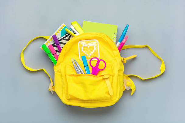 Назад в школу, концепция образования. Желтый рюкзак со школьными принадлежностями - ноутбук, ручки, линейка, калькулятор, ножницы изолированы на сером фоне. Вид сверху. Копировальное пространство Плоская композиция
 - Фото, изображение