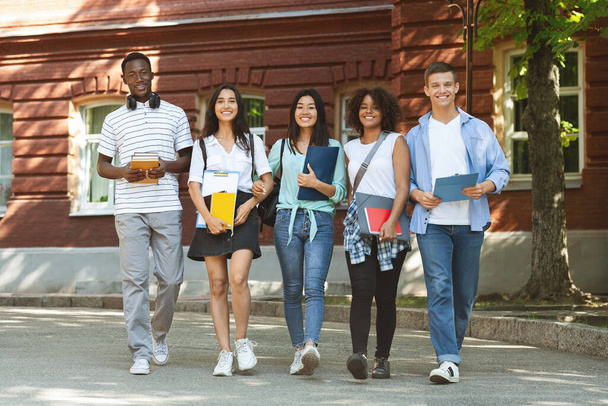 Estudantes multiculturais felizes caminhando juntos perto do campus universitário
 - Foto, Imagem