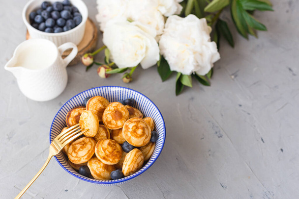 Mini ontbijtgranen pannenkoeken met bosbessen in een kom op grijze achtergrond. Trendy food concept, Ontbijt tijd voor kinderen. Menu, recept, bovenaanzicht of plat leggen - Foto, afbeelding