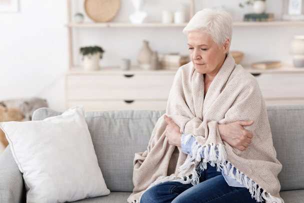 Senior lady sitting on couch covered with blanket, shivering with high temperature - Foto, Bild