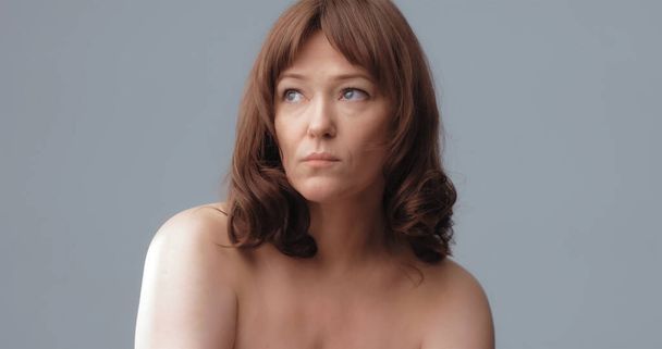 Pensive pretty naked woman isolated on gray background. Mature beautiful looking at side on copy space. Spa and wellness concept. Aging process concept - Photo, image