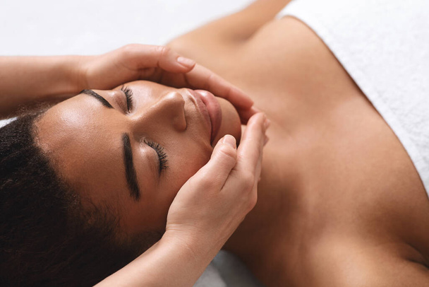 Primo piano di mani terapeuta facendo massaggio facciale per la signora nera - Foto, immagini