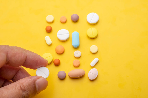 hand holding pill, many different pills on yellow background  - Photo, Image