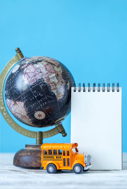 Back to school concept. Yellow school bus toy model and empty blank with globe and school supplies - Foto, Imagem