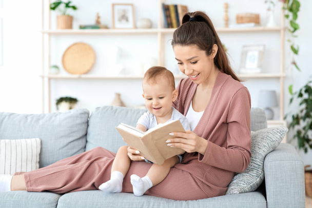 Early development. Millennial mom reading book to her toddler baby at home - Photo, Image