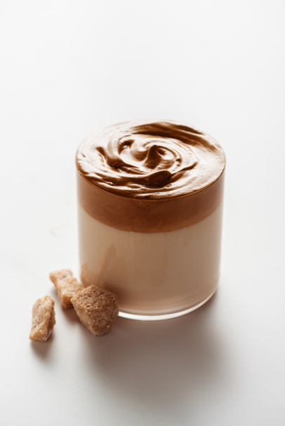 delicious Dalgona coffee in glass near brown sugar on white background - Foto, Imagen
