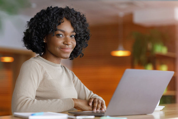 Smiling black lady using laptop at cafe - Foto, afbeelding