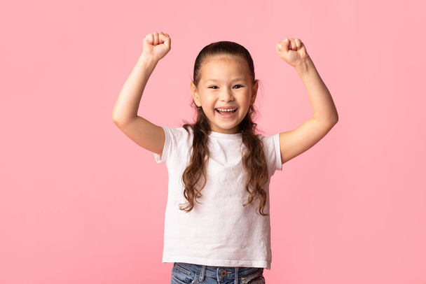 Boldog kis ázsiai lány felemeli öklét, hogy a győztes gesztus - Fotó, kép