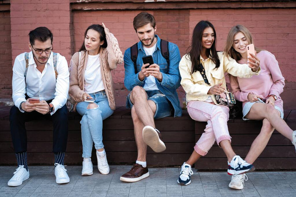 Modern Generation. Group of young people using gadgets, sitting on stairs outdoor, free space - Foto, afbeelding