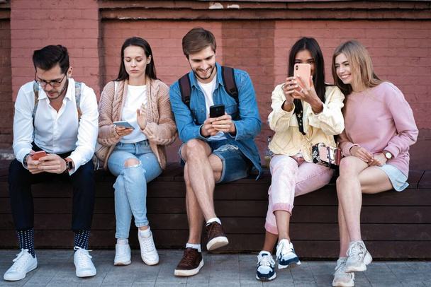 Generación moderna. Grupo de jóvenes que utilizan gadgets, sentado en las escaleras al aire libre, espacio libre
 - Foto, Imagen