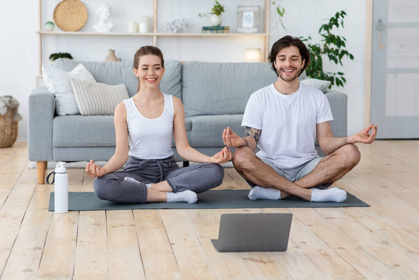 Healthy young couple meditating at home, looking at laptop screen - Фото, изображение