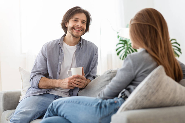 Ευτυχισμένος τύπος πίνει καφέ και μιλάει με την κοπέλα του στο σπίτι. - Φωτογραφία, εικόνα