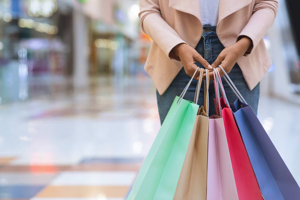 Mujer negra irreconocible de pie con un montón de bolsas de compras de colores en el centro comercial
 - Foto, Imagen