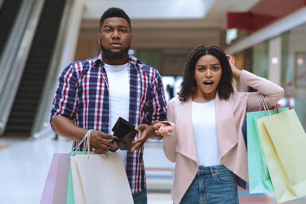 Shopaholics. Verwirrtes schwarzes Paar demonstriert leere Geldbörse und gibt alles Geld für Einkäufe aus - Foto, Bild