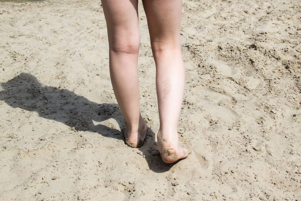 Klein meisje dat blootsvoets over het strand loopt. Een geweldige compositie voor het ontwerp met een klein meisje met vieze benen lopen op zand. Schaduw van het meisje - Foto, afbeelding