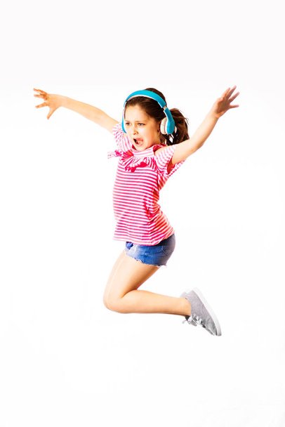 Poco saltando y gritando pequeña chica caucásica con auriculares sobre fondo blanco
 - Foto, Imagen