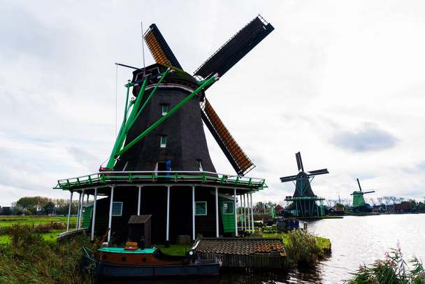 Voll funktionsfähige historische und authentische Zaandam-Mühlen am Wasserkanal im Dorf Zaanstad. Windmühlen von Zaanse Schans und berühmte Kanäle der Niederlande, Europa. - Foto, Bild