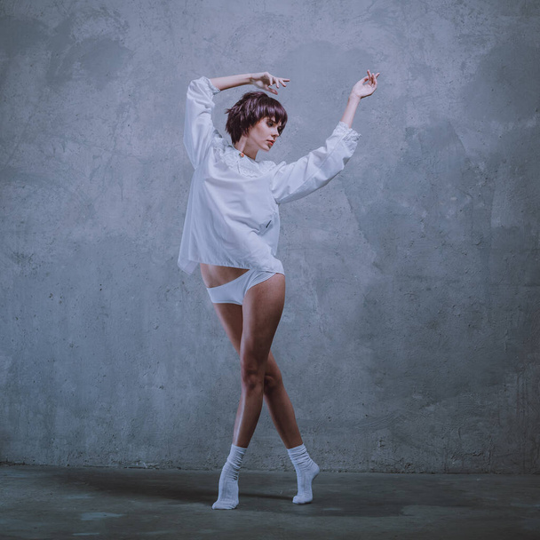 Young beautiful girl with short hair, in white lingerie, a white shirt and white socks, in a studio with a gray background. - Fotografie, Obrázek